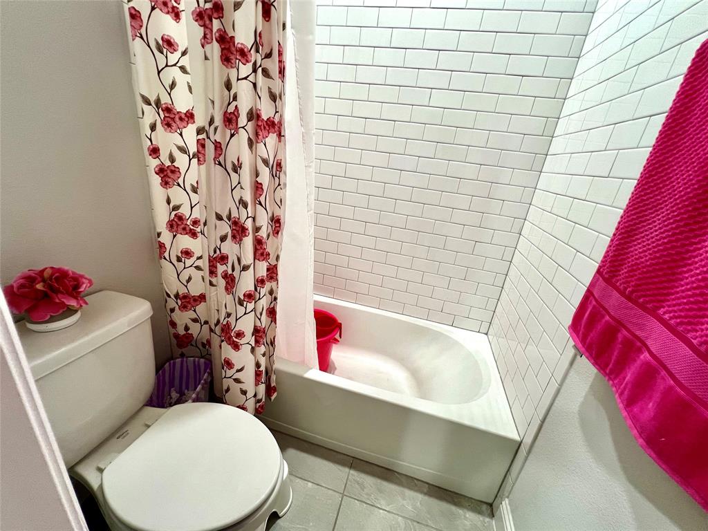 Bathroom featuring shower / bathtub combination with curtain, tile patterned floors, and toilet