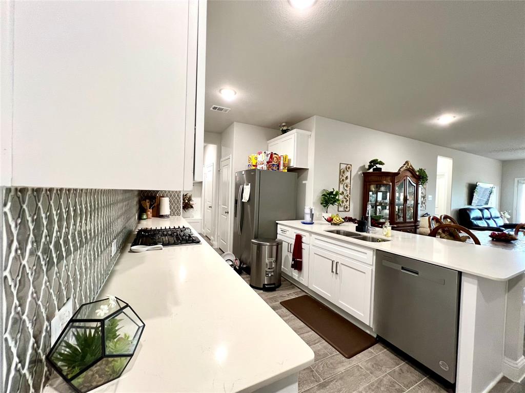 Kitchen with tasteful backsplash, sink, white cabinetry, kitchen peninsula, and stainless steel appliances
