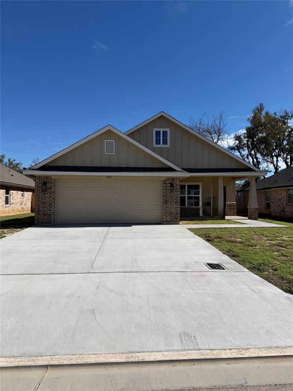 Exterior featuring a gable roof, vertical siding, brick accents, and a concrete driveway