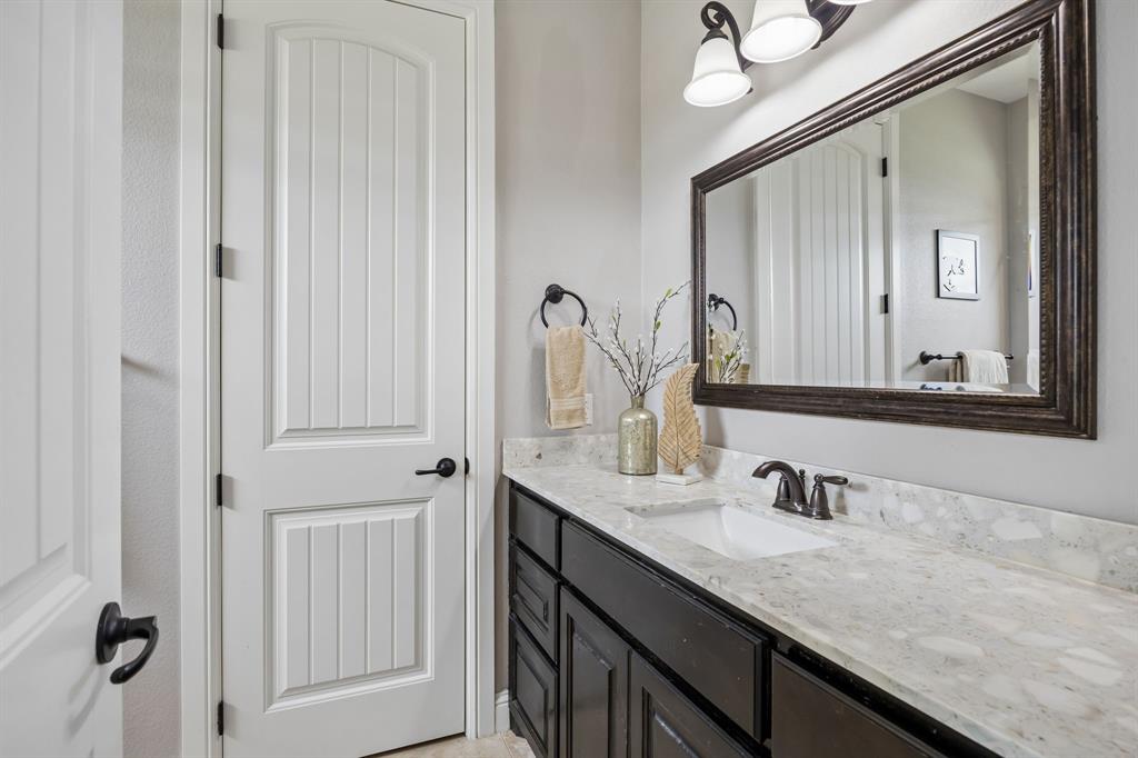 Vanity featuring a stone-composite countertop with an integrated basin, dark-finish cabinetry, a framed wall mirror, and dual-light fixture