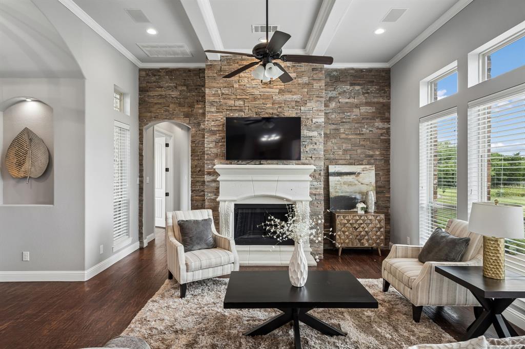 Living area featuring a floor-to-ceiling stone fireplace surround, coffered ceiling, wood-finish flooring, an arched display niche, and large windows