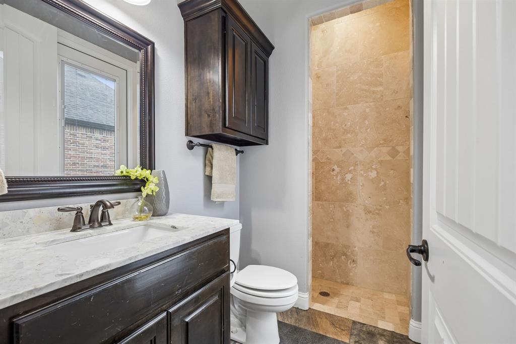 Bathroom featuring a dark wood vanity with a light stone countertop, a framed wall mirror, a matching wall-mounted cabinet, and a walk-in shower with tile surround