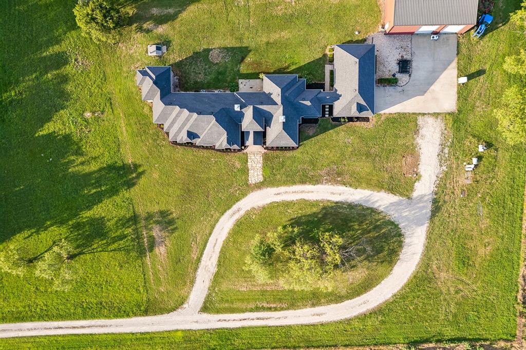 Aerial perspective featuring a multi-gabled roofline, expansive acreage, a circular gravel driveway, and a detached outbuilding