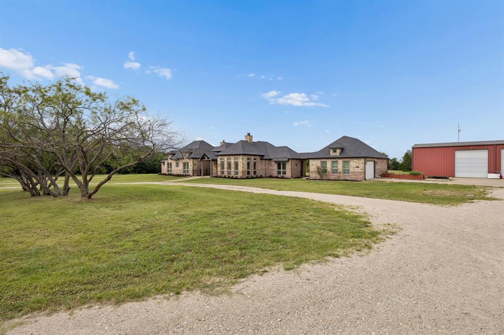 Single-story brick and stone residence featuring a multi-gabled roofline, expansive lawn, gravel driveway, and detached metal workshop