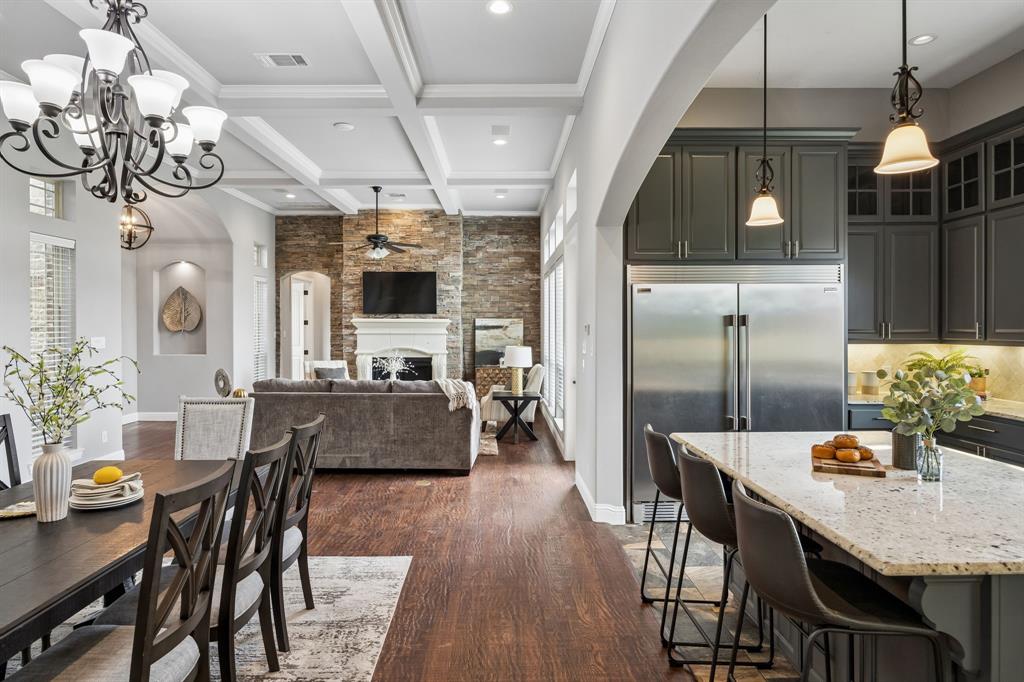 Coffered ceiling, stone-surround fireplace, dark-finish cabinetry, stone-topped island, and wood-finish flooring