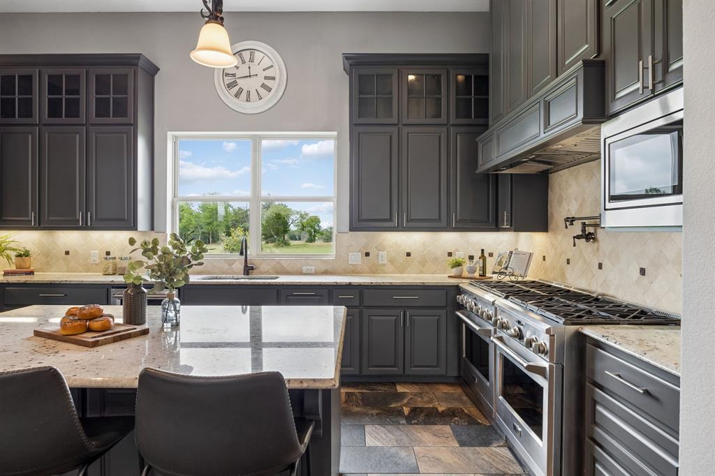Kitchen featuring shaker-style cabinetry, a central island with stone-finish countertop, professional-grade stainless steel range, diamond-pattern tile backsplash, and multi-tone tile flooring