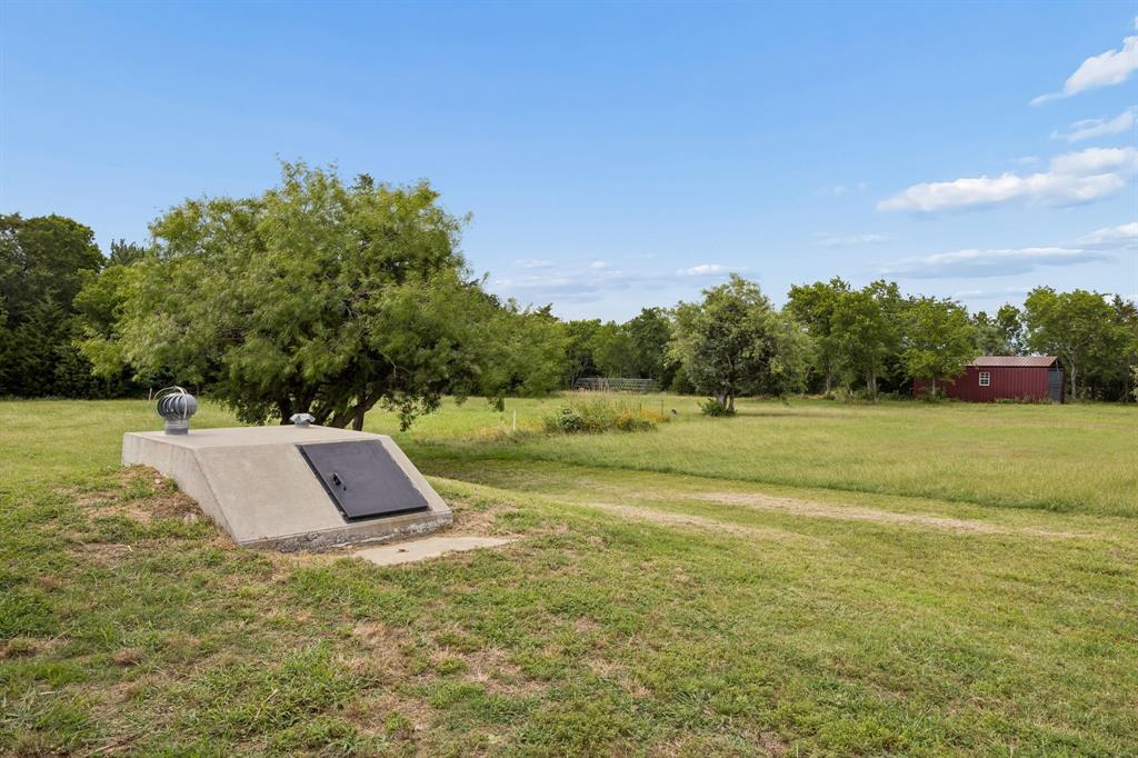 Expansive parcel featuring a concrete storm shelter with a metal access door and turbine vent, mature trees, and a detached storage structure