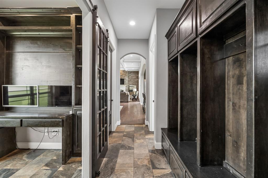 Built-in dark wood cabinetry with integrated desk space, custom mudroom lockers, sliding glass-paneled barn door, arched hallway entry, and stone-finish tile flooring