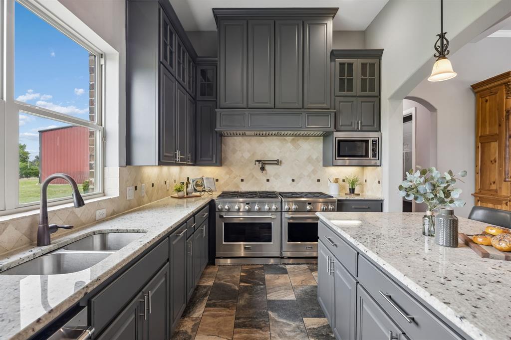 Kitchen featuring charcoal cabinetry, light stone countertops, stainless steel dual-range appliances, a tile backsplash with decorative accents, and slate-finish flooring