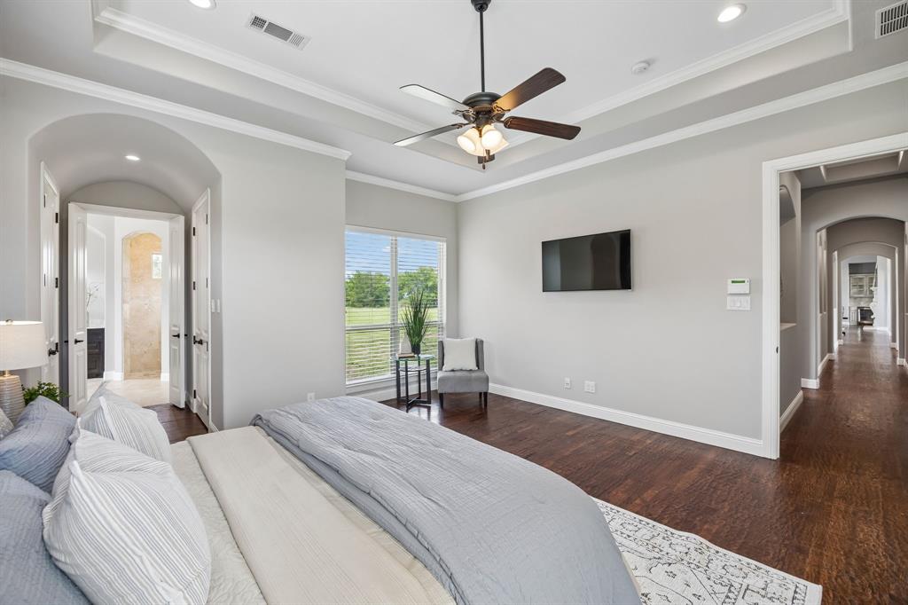 Tray ceiling with a central multi-blade ceiling fan, arched doorways, wood-finish flooring, and natural light from a large window
