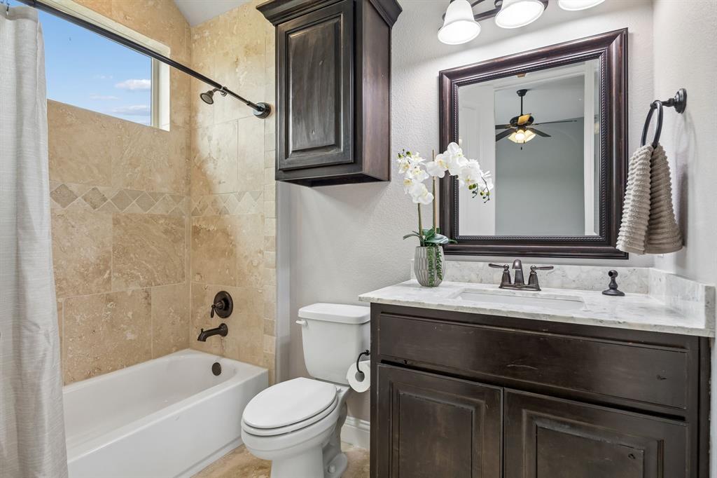 Bathroom featuring a tub-shower combination with natural stone wall tile, dark-finish cabinetry, a stone-top vanity with an undermount sink, and oil-rubbed bronze fixtures