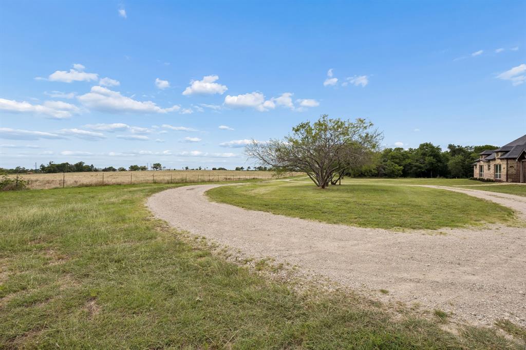 Expansive grounds featuring a circular gravel driveway, mature trees, open pasture, and wire perimeter fencing