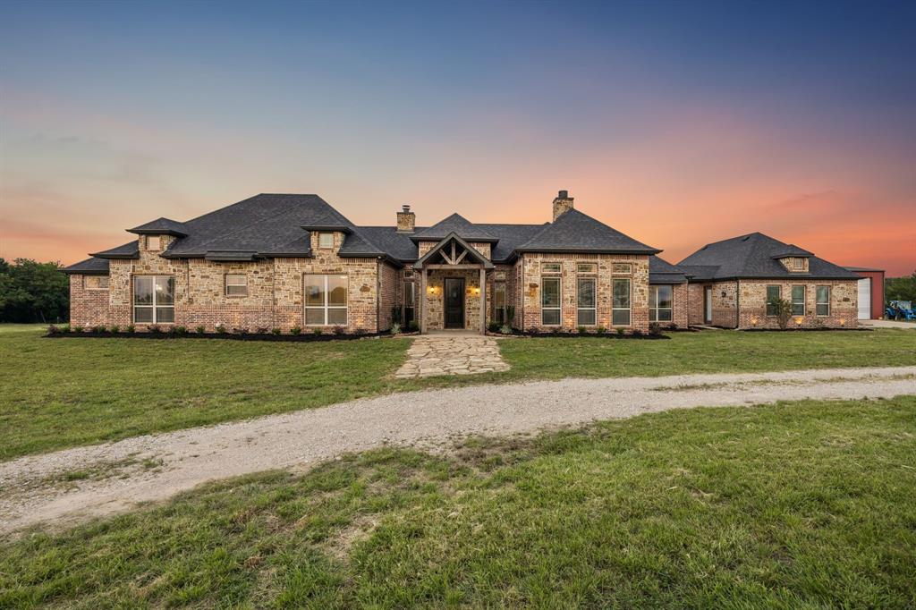 Single-story residence featuring a stone and brick facade, multi-gabled roofline, covered entryway with timber-frame accents, and a natural stone walkway