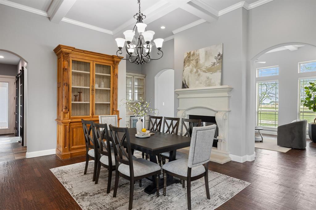 Dining area featuring wood-finish flooring, coffered ceilings, a traditional-style fireplace with stone mantel, ornate chandelier lighting, and arched doorways