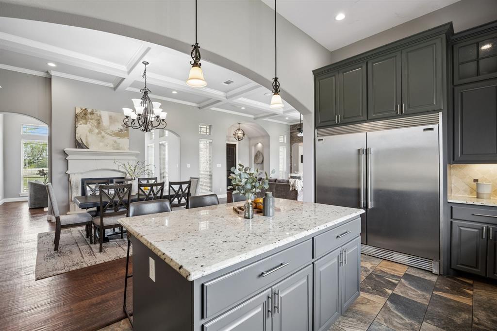Kitchen featuring dark cabinetry, stone-topped central island, stainless steel refrigerator, stone tile flooring, and coffered ceilings