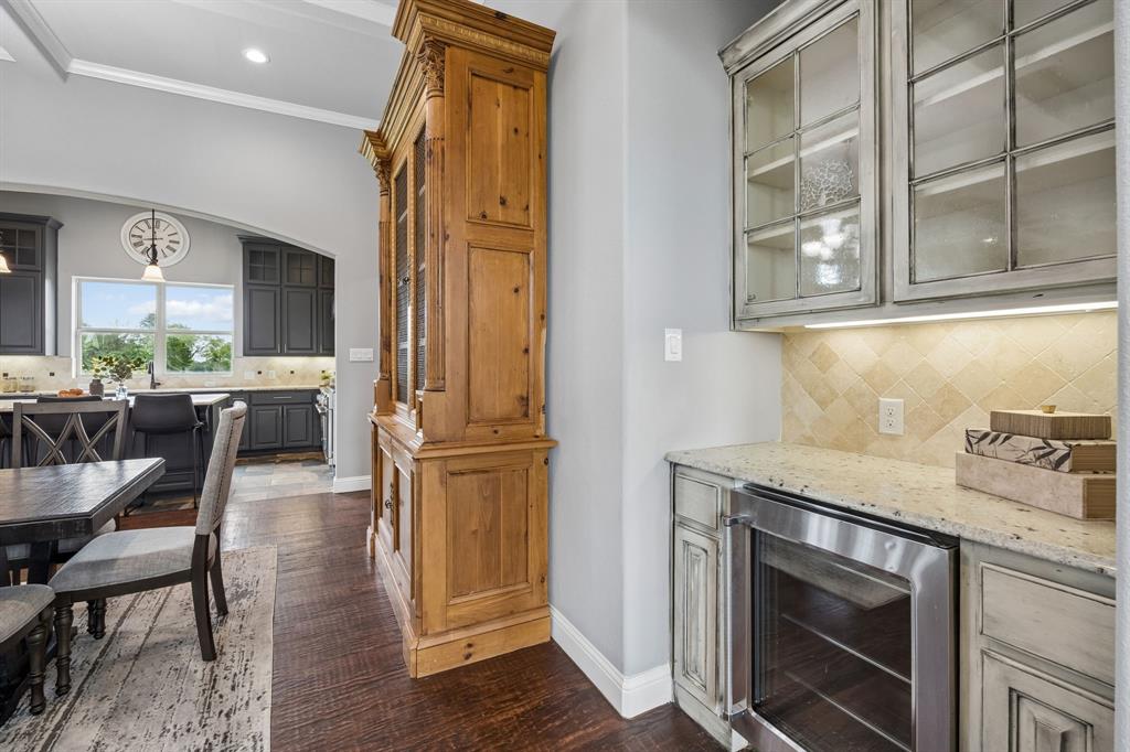Custom built-in wood cabinetry, integrated wine refrigerator, glass-front upper cabinets, stone tile backsplash, and wood-finish flooring