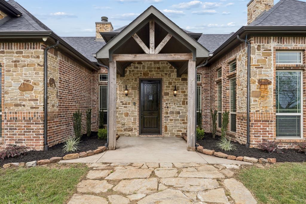 Stone and brick exterior facade featuring a covered entryway with timber beam accents, a paneled wood front door, and a natural stone walkway