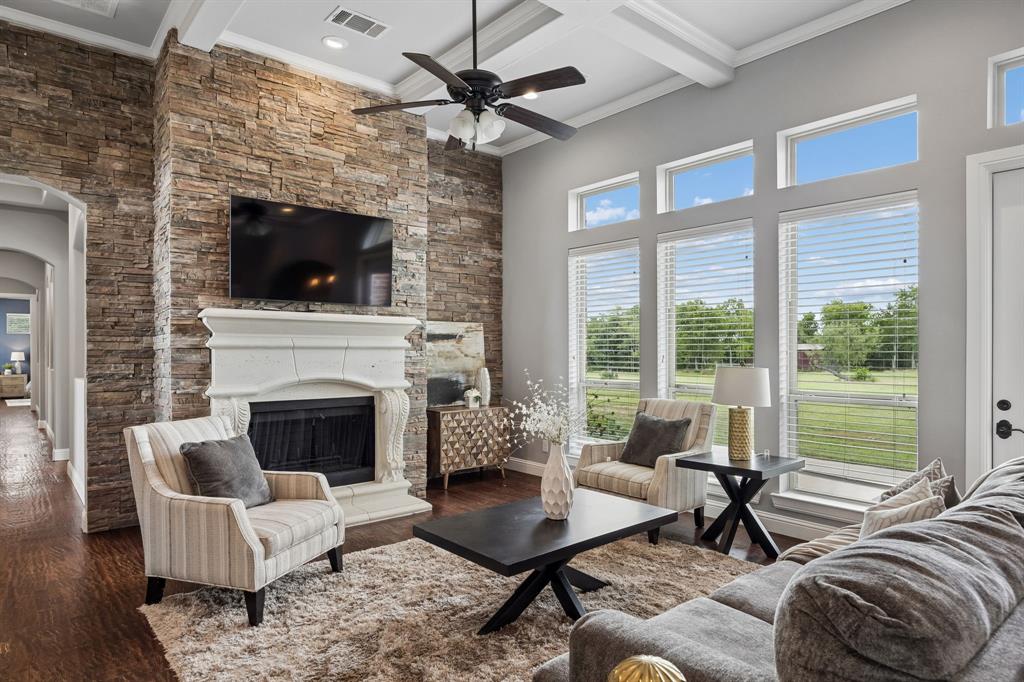 Living area featuring a floor-to-ceiling stacked stone fireplace, ornate mantle, coffered ceiling, tall windows with transom accents, and wood-finish flooring