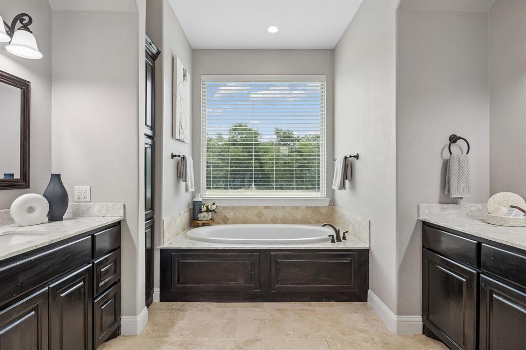 Bathroom featuring dual dark-finish vanities with stone countertops, a deep soaking tub with a stone-tile surround, and tile flooring