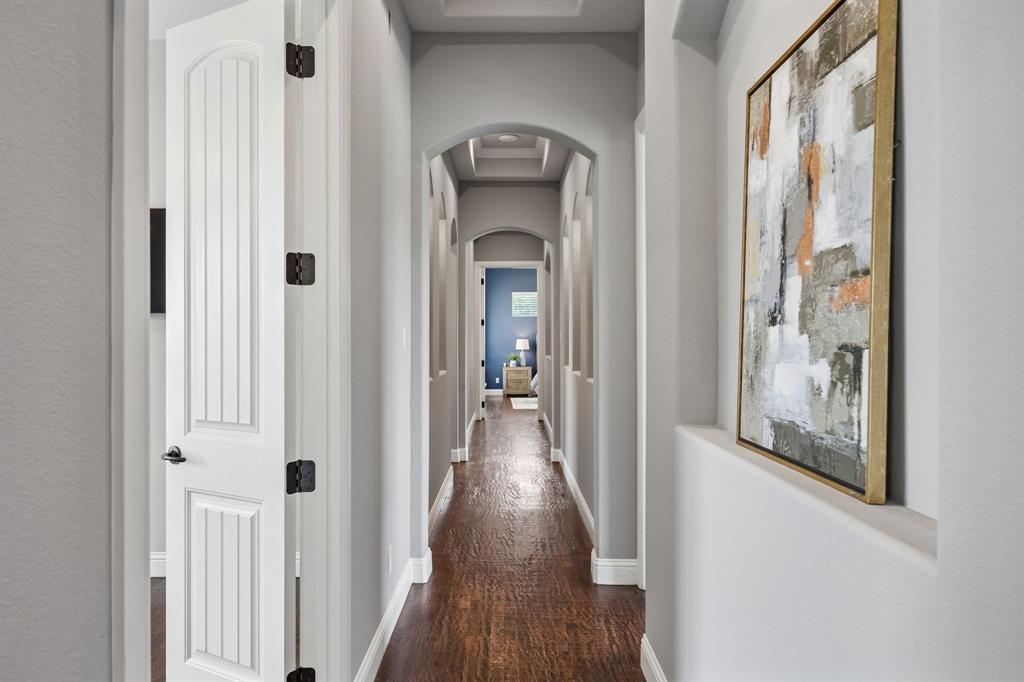 Hallway featuring wood-finish flooring, recessed wall niches, arched architectural detailing, and coffered ceiling elements