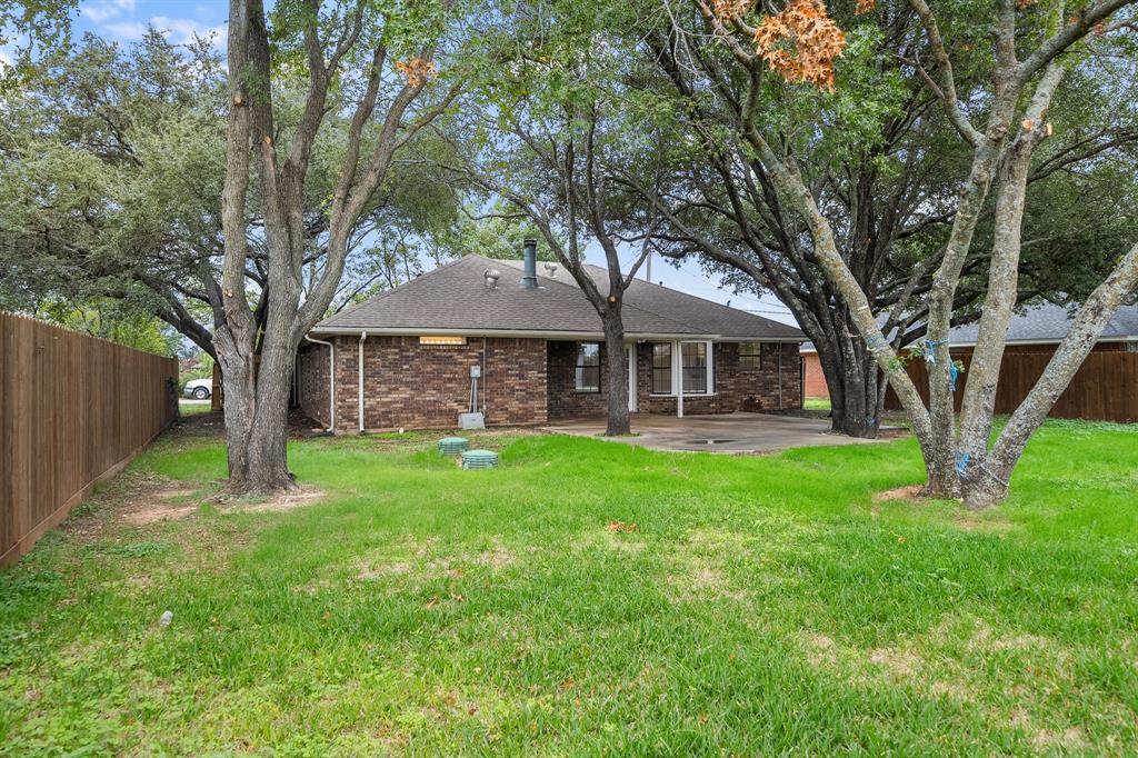 Rear exterior featuring brick siding, a concrete patio, mature trees, and a wooden privacy fence