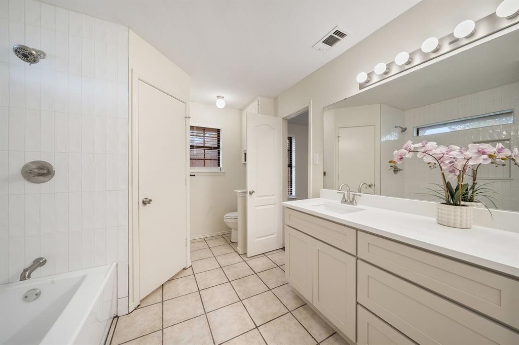 Bathroom featuring tile flooring, a white vanity with an integrated countertop, a full-width wall mirror, and a tub-shower combination with floor-to-ceiling tile surround