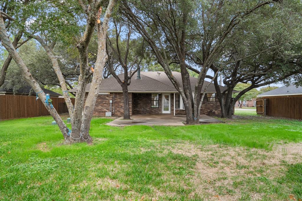 Backyard featuring a concrete patio, brick exterior, wood privacy fencing, and mature canopy trees