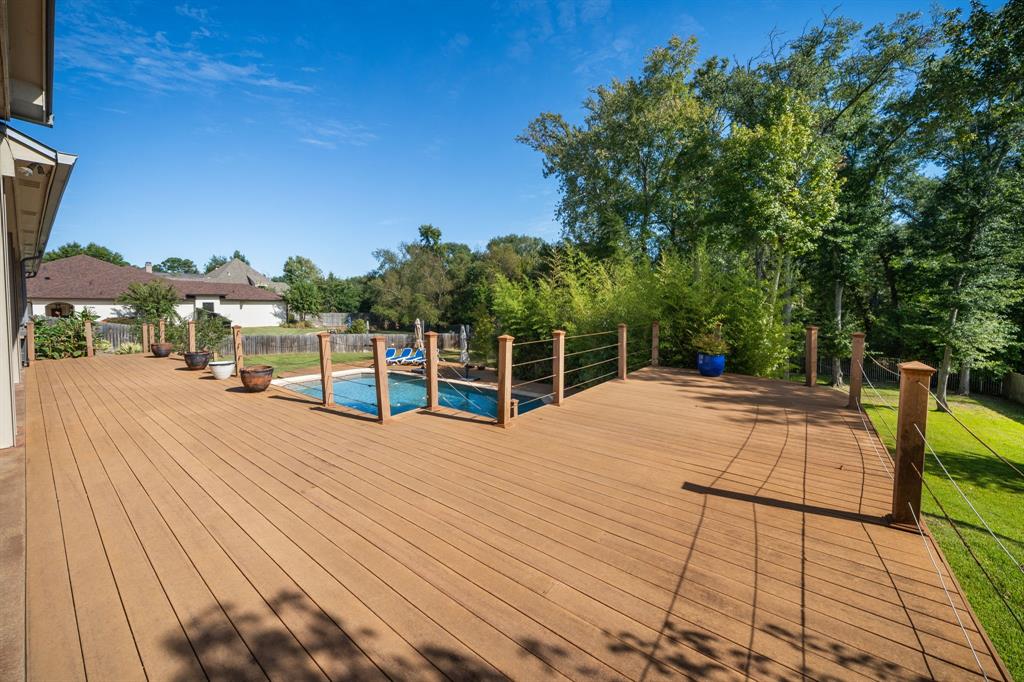 Expansive wood-finish deck featuring a sunken in-ground swimming pool, horizontal cable railing system, and mature tree-lined perimeter