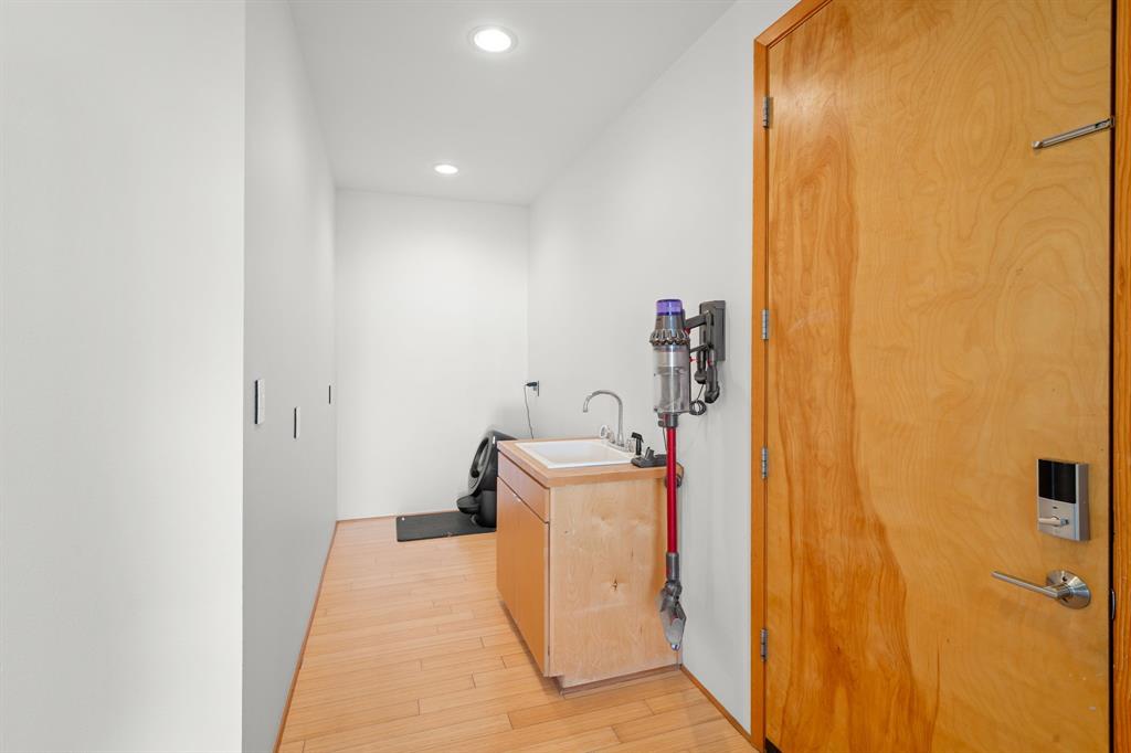Utility area featuring wood-finish flooring, recessed lighting, a wood-cabinet vanity with a rectangular sink, and a solid wood door with integrated electronic lock hardware