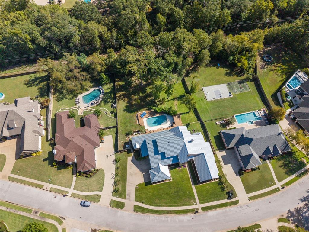 Aerial perspective featuring a multi-gabled residence with a metallic roof, rear swimming pool, concrete driveway, and expansive grass lawn