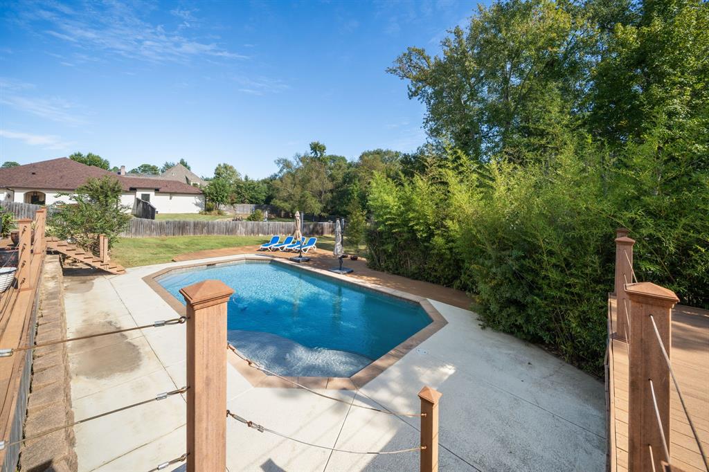In-ground swimming pool with concrete decking, surrounded by mature trees and wood-finish railings with cable tension detailing