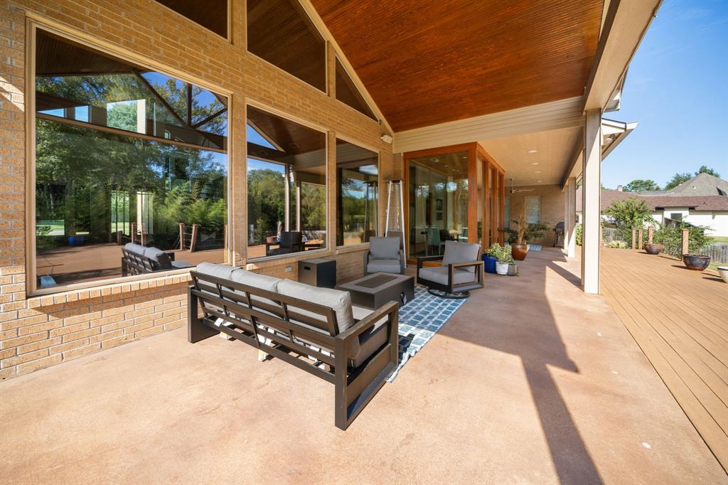 Covered patio featuring a high, wood-planked ceiling, expansive floor-to-ceiling windows, brick exterior walls, and a wood-finish deck