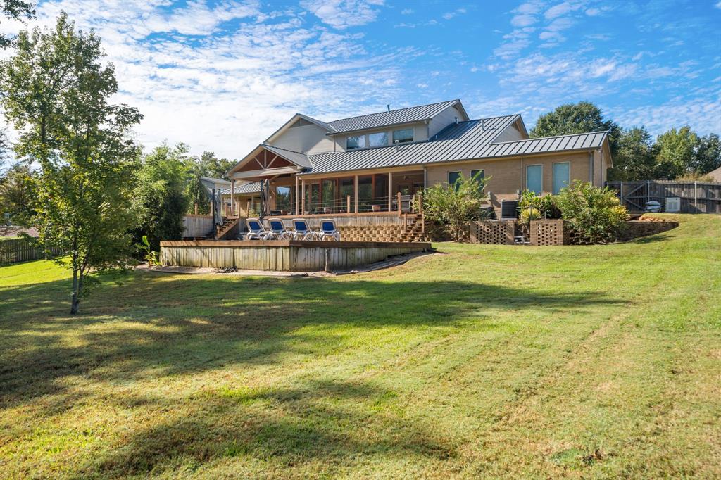Multi-level residence featuring a metal roof, expansive wood deck, and masonry exterior walls, situated on a large lot with mature landscaping