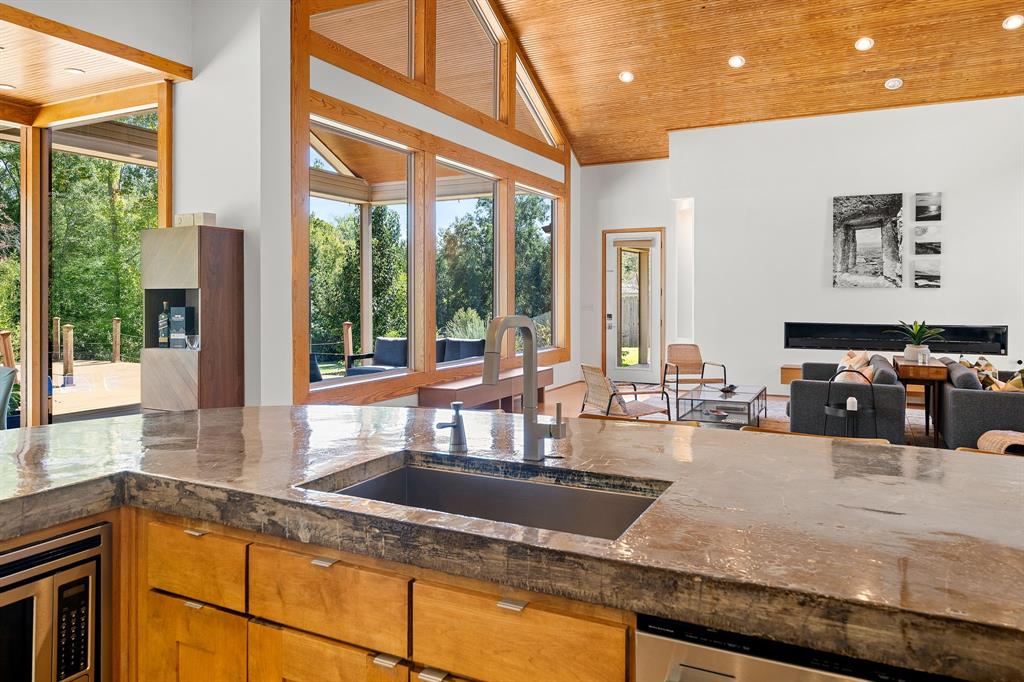 Kitchen featuring a stone countertop, an undermount sink with a gooseneck faucet, custom wood cabinetry, a vaulted wood-paneled ceiling, and expansive floor-to-ceiling windows