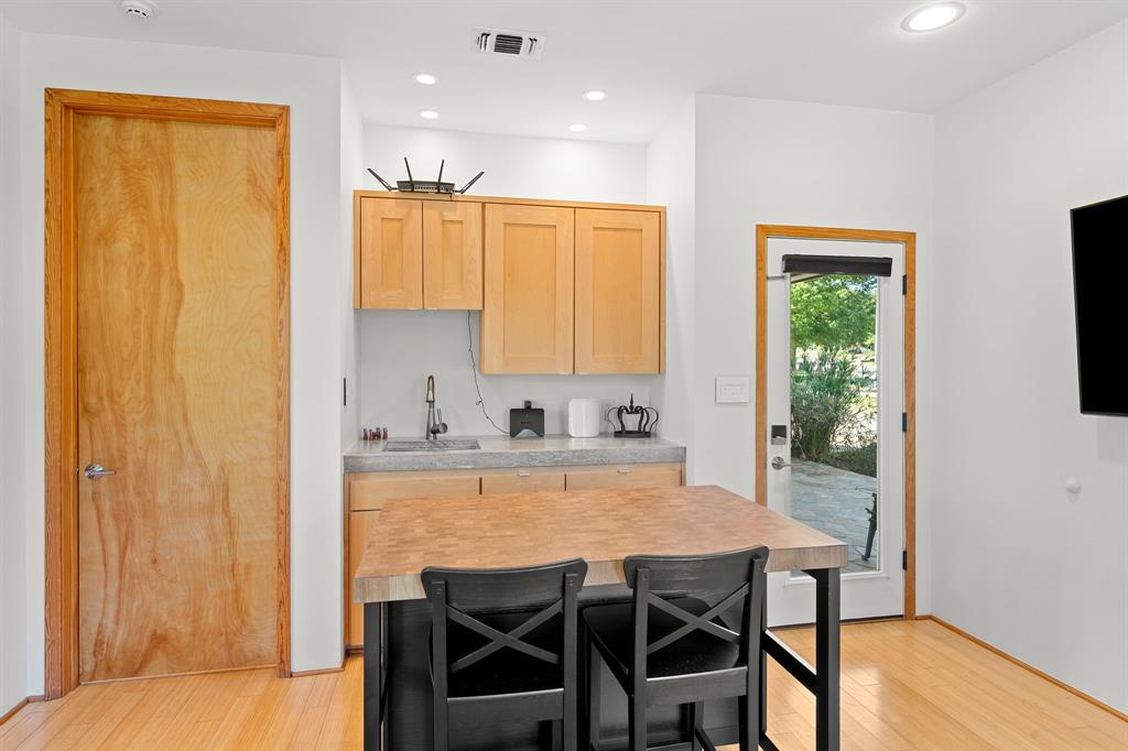 Custom kitchenette featuring light wood cabinetry, stone-surface countertop with an integrated sink, recessed lighting, and wood-finish flooring