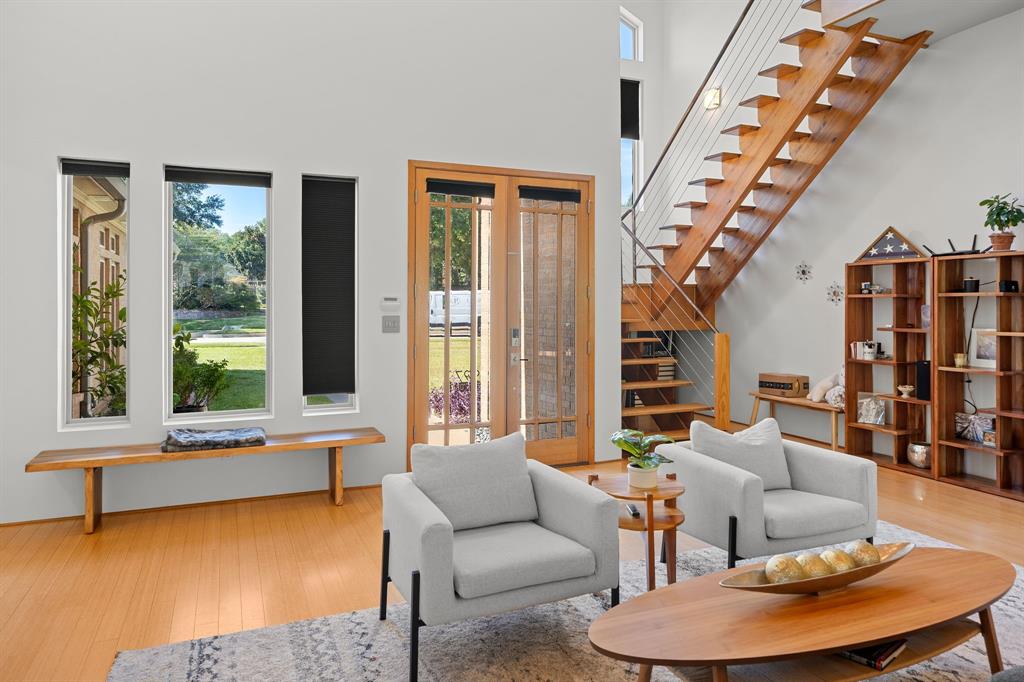 Double-height living area featuring an open-riser staircase with metal cable railing, floor-to-ceiling windows, and wood-finish flooring