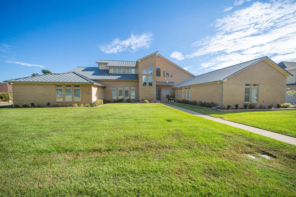 Contemporary exterior featuring a light-toned brick facade, standing seam metal roof, multi-level architectural design, and geometric windows set within an expansive grass lawn Contemporary exterior featuring a light-toned brick facade, standing seam metal roof, multi-level architectural design, and geometric windows set within an expansive grass lawn