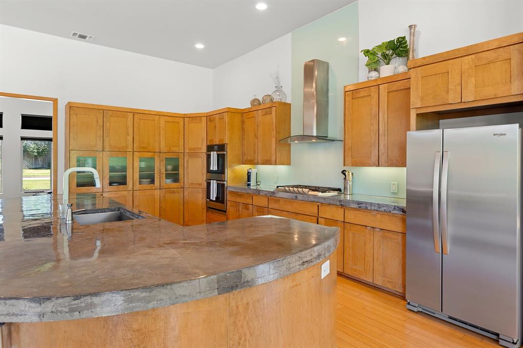 Kitchen featuring wood cabinetry, concrete countertops, stainless steel built-in double ovens, stainless steel range hood, and wood-finish flooring