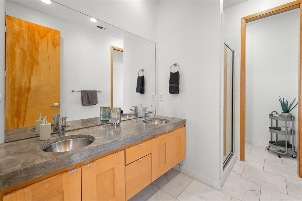 Double vanity featuring natural wood cabinetry, integrated concrete-style countertop, dual stainless steel drop-in sinks, and a full-width wall mirror