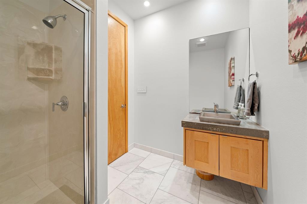 Bathroom featuring a shower with a glass enclosure, wall-mounted wood vanity, rectangular vessel sink, concrete-finish countertop, and large-format tile flooring