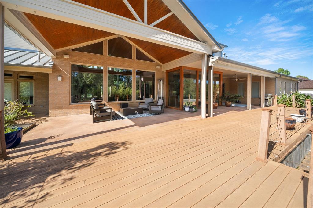 Expansive wood-finish deck featuring a covered patio area, vaulted ceilings with wood inlay, large picture windows, and cable railing
