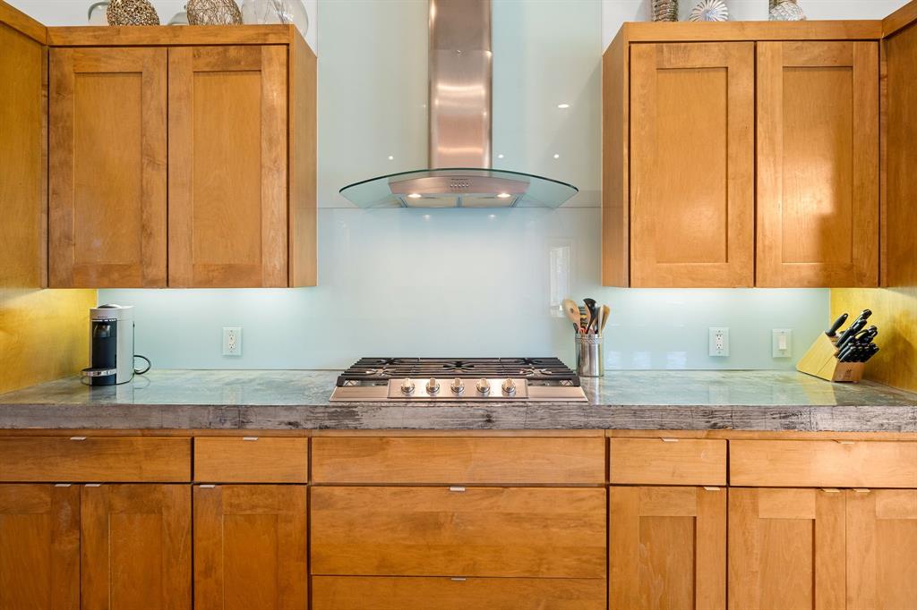 Custom cabinetry with shaker-style doors, stone countertop, glass backsplash, stainless steel gas cooktop, and glass canopy range hood