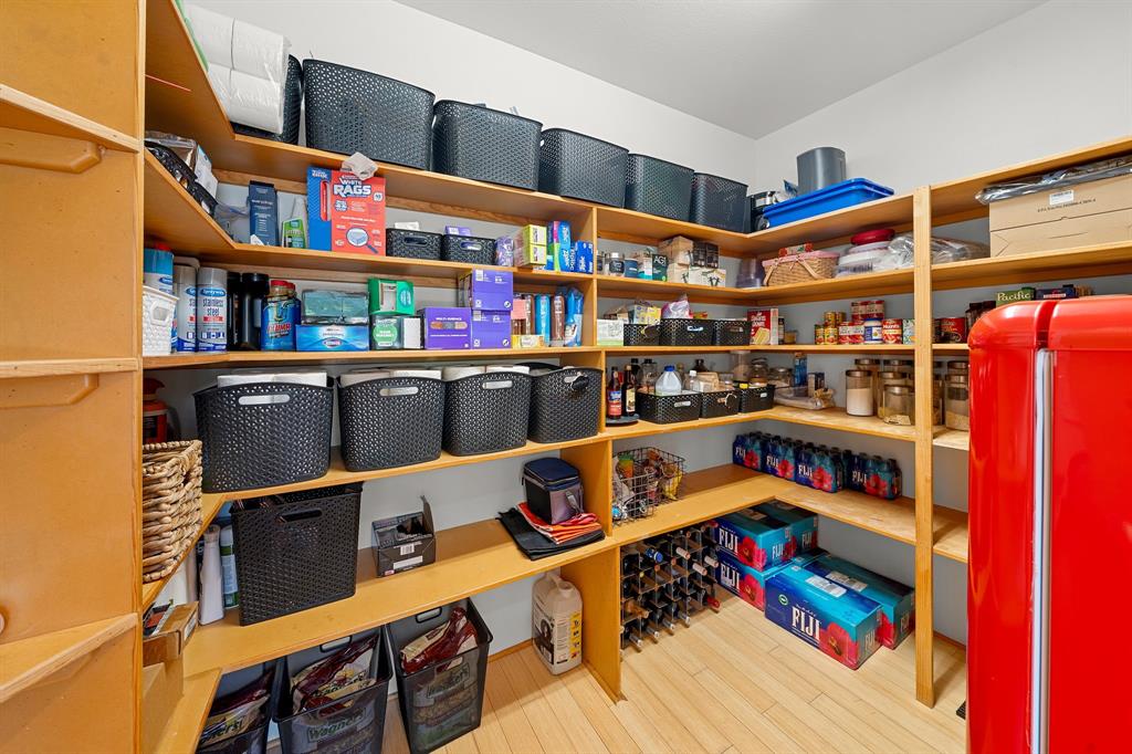 Walk-in pantry featuring extensive wrap-around wooden shelving, light-toned wood-finish flooring, and a dedicated built-in wine rack