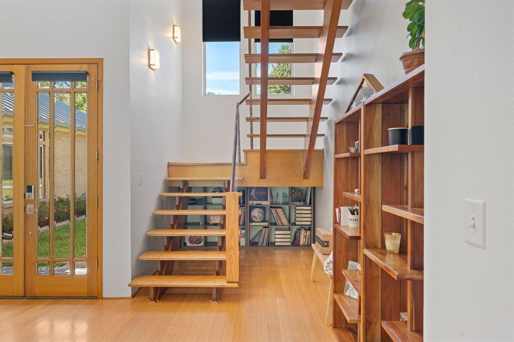 Open-tread staircase with wood finish, integrated cube shelving, wood-finish flooring, multi-pane glass entry door, and vertical window configuration