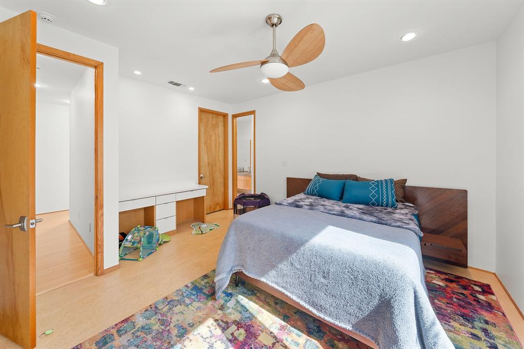 Room featuring wood-finish flooring, recessed lighting, a modern ceiling fan, a built-in white desk with drawer storage, and a custom wood-panel headboard