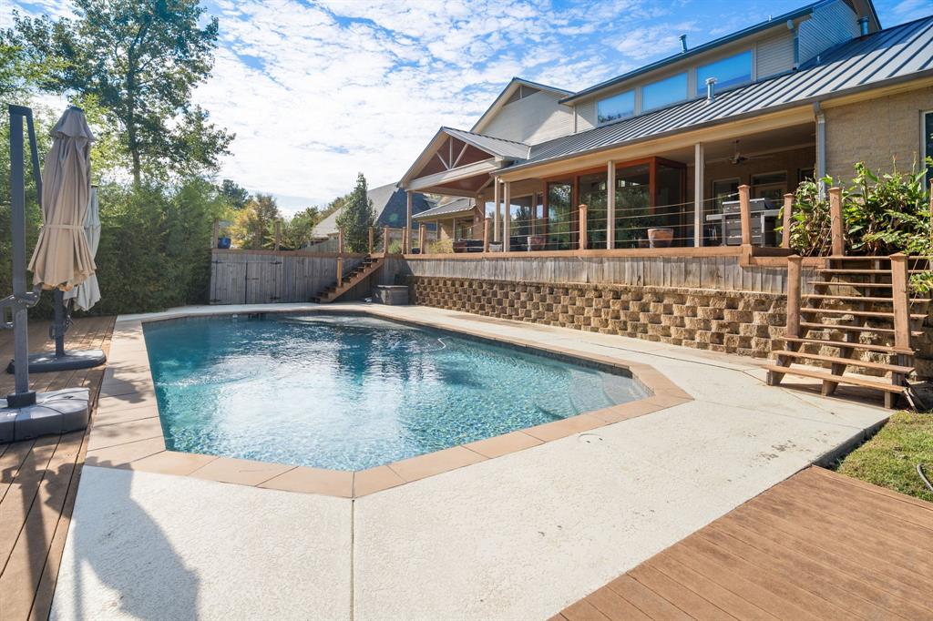 Inground swimming pool with concrete decking, tiered retaining wall, elevated wooden deck, and covered patio space
