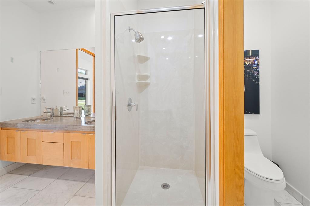 Walk-in shower with glass enclosure, floating vanity with dual sinks, stone-finish countertop, and tile flooring