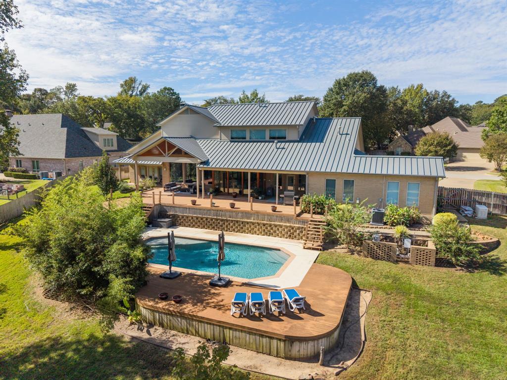 Multi-level exterior featuring a standing-seam metal roof, expansive elevated wood deck, inground swimming pool with concrete surround, and structured retaining walls