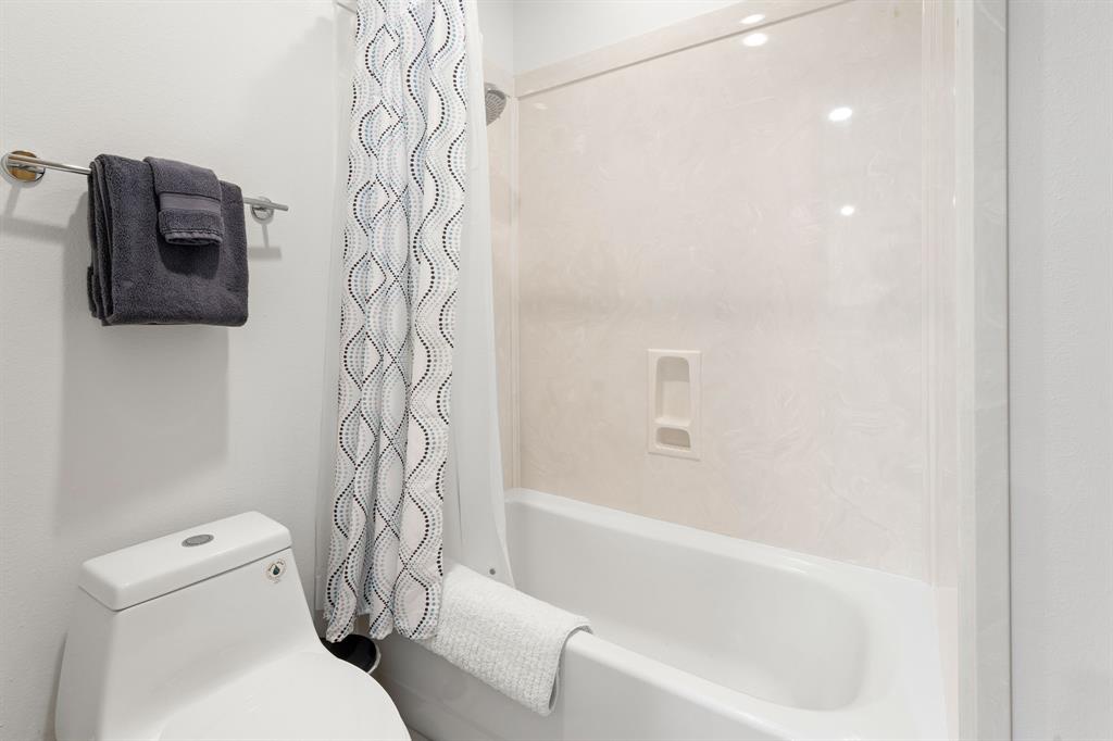 Full-height tub and shower surround with integrated storage niche, one-piece dual-flush toilet, and wall-mounted metal towel rack