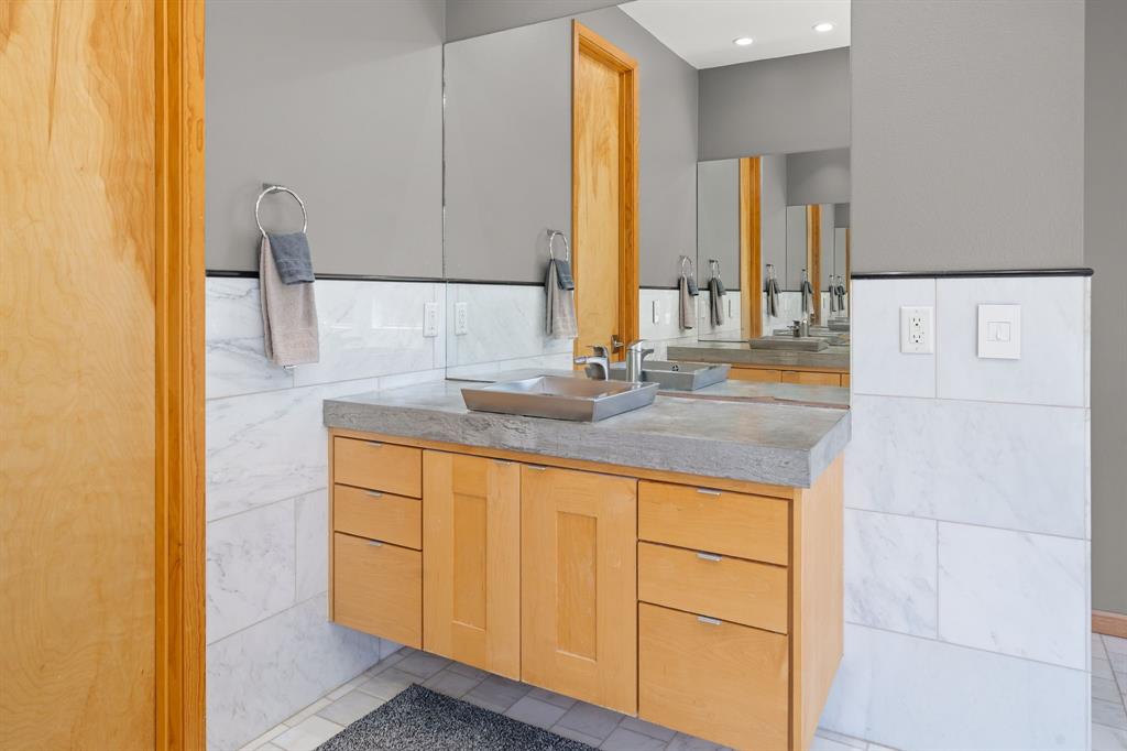Floating wood cabinetry vanity featuring a concrete countertop, square vessel sink, polished chrome faucet, and floor-to-ceiling tile surround